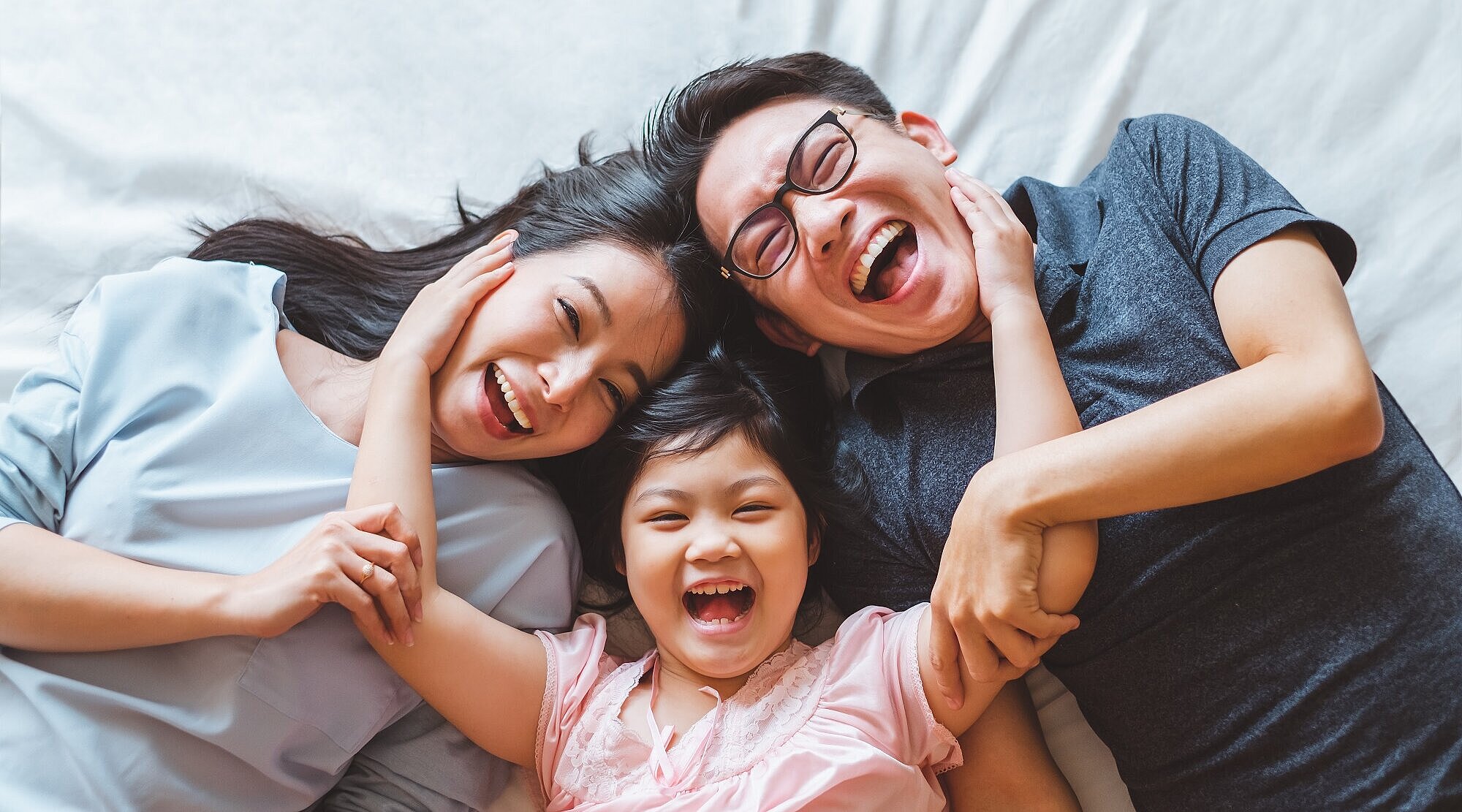 Foto: Asiatische Familie liegt auf einem Bett und lacht in die Kamera