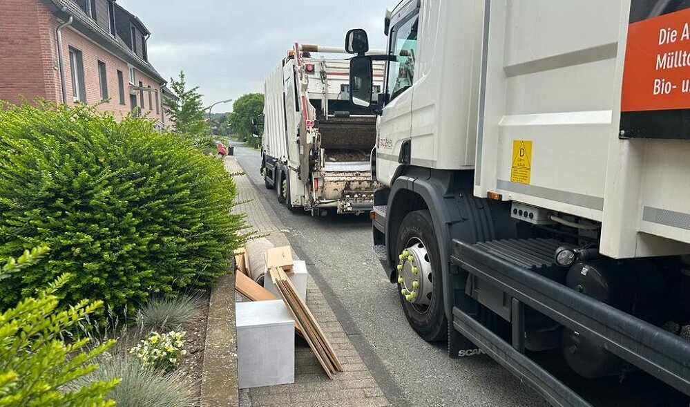 Foto: Müllfahrzeuge neben einem Bürgersteig mit Sperrmüll"